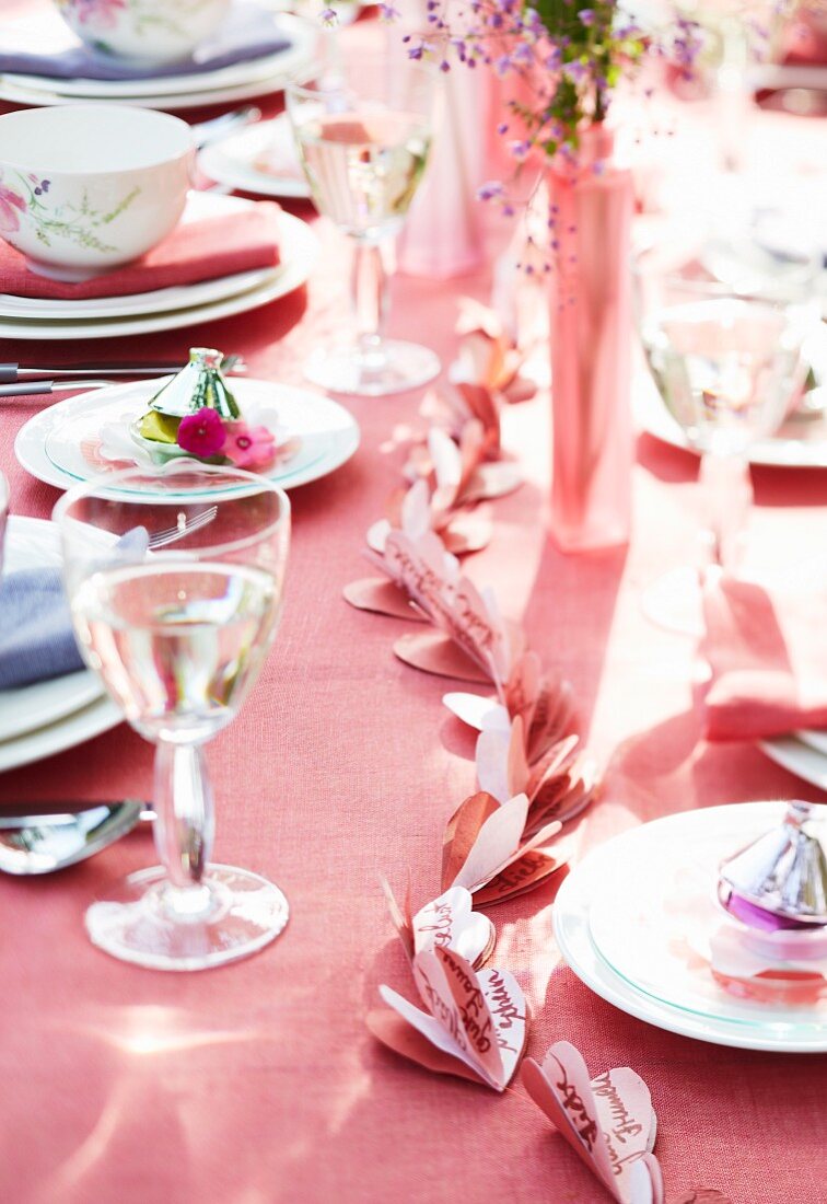 A table laid with a pink tablecloth and a pink paper garland