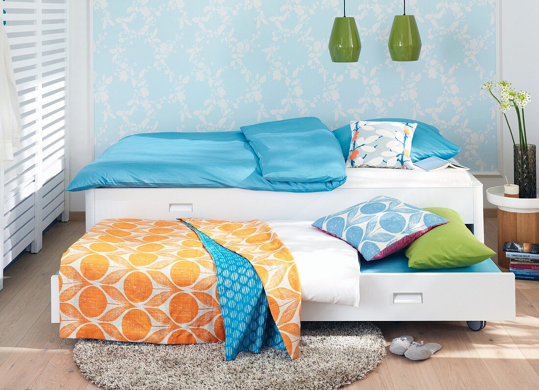 Bettwäsche im bunten Mustermix auf ausziehbarem Gästebett, im Hintergrund zartflorale Wandgestaltung