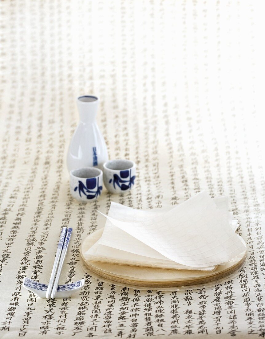 Rice paper on a wooden board, with chopsticks and a sake set to one side