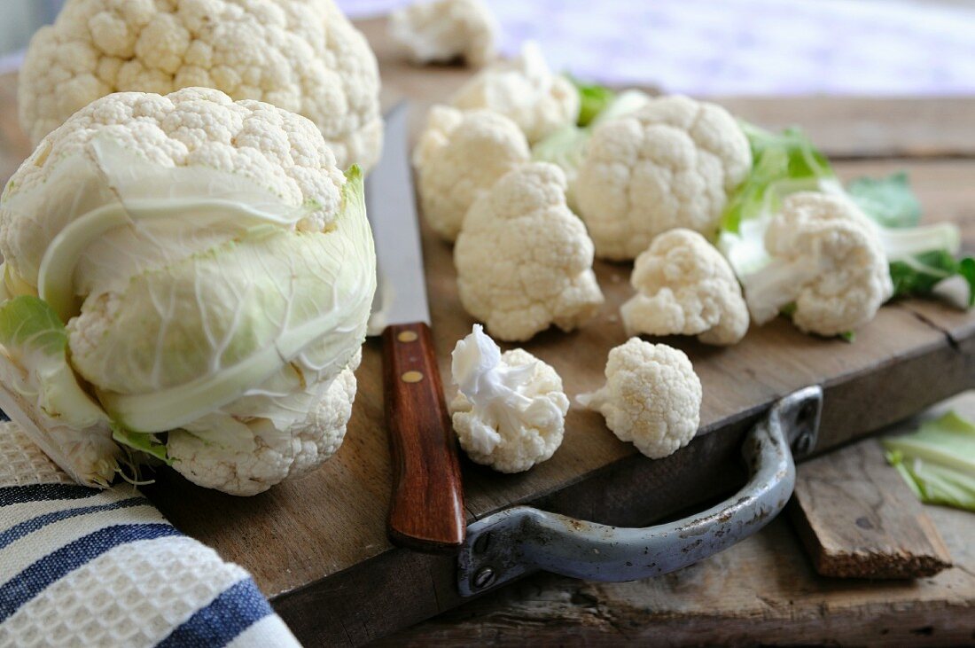 A whole cauliflower and individual florets on a wooden chopping board