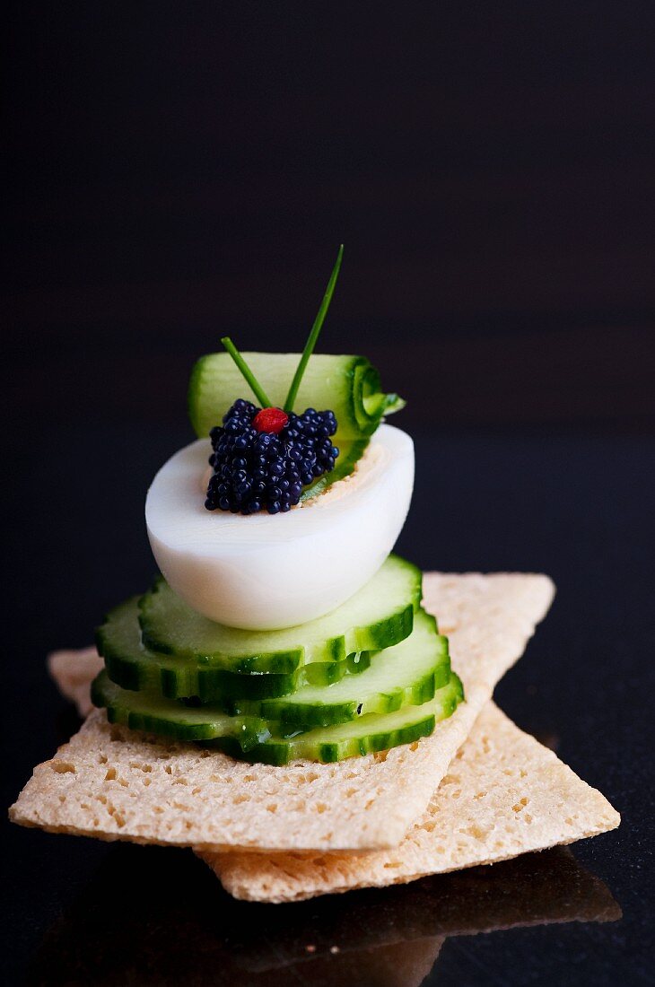 Gekochtes Ei mit Seehasenkaviar und Gurkenscheiben auf Knäckebrot