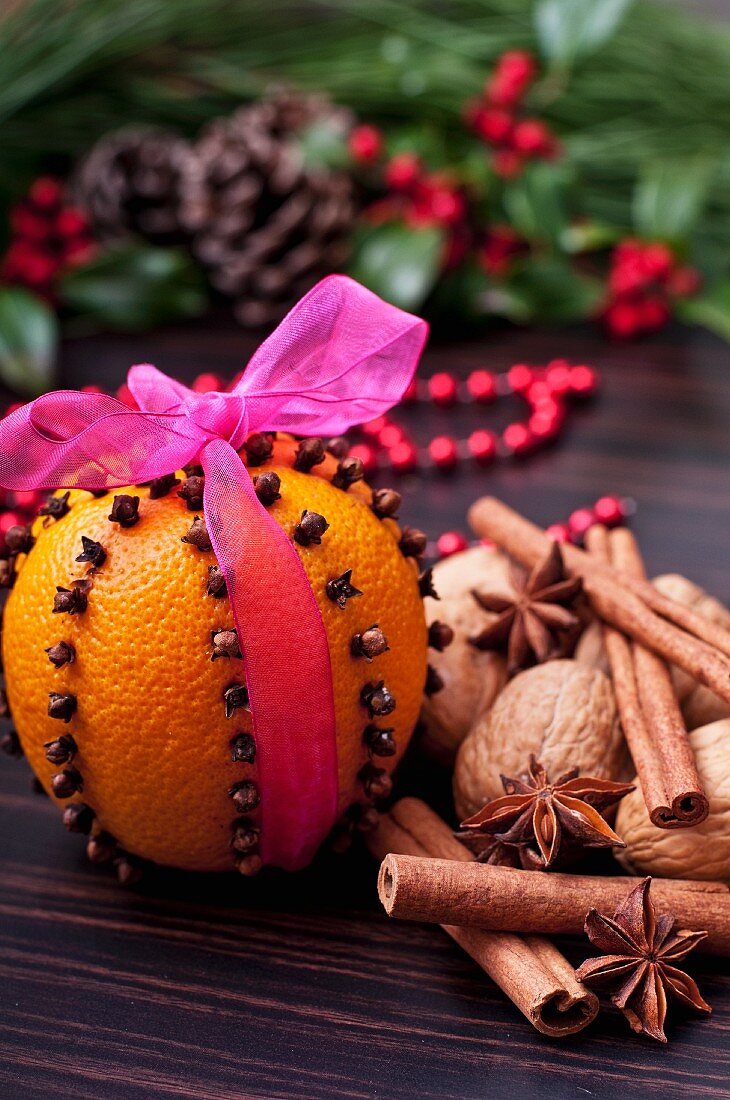 Gespickte Orange mit pinkfarbenem Geschenkband, Walnüsse und Gewürze