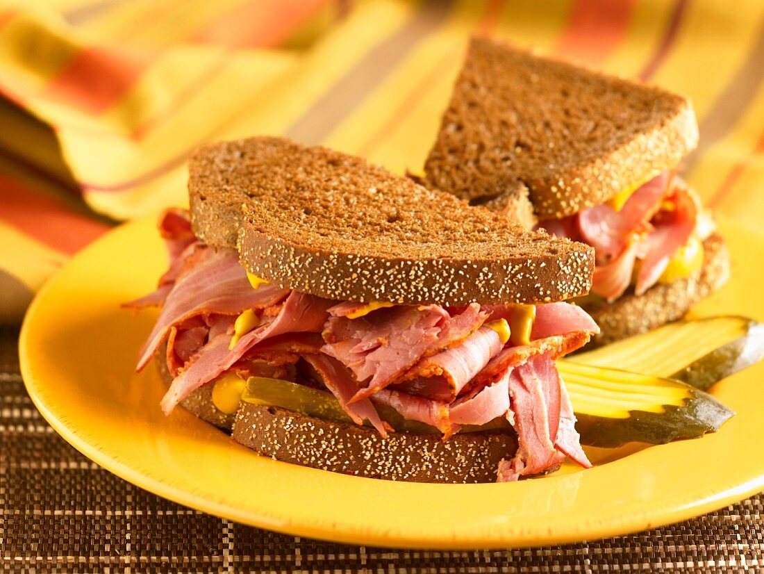 Corned Beef Sandwich with Mustard and Pickles on Pumpernickel Bread; Halved on a Yellow Plate