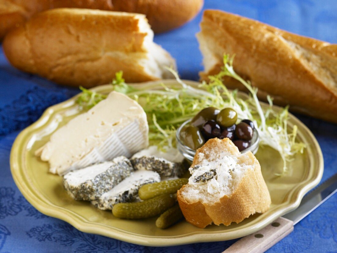 Käseplatte mit Essiggurken, Oliven und Baguette