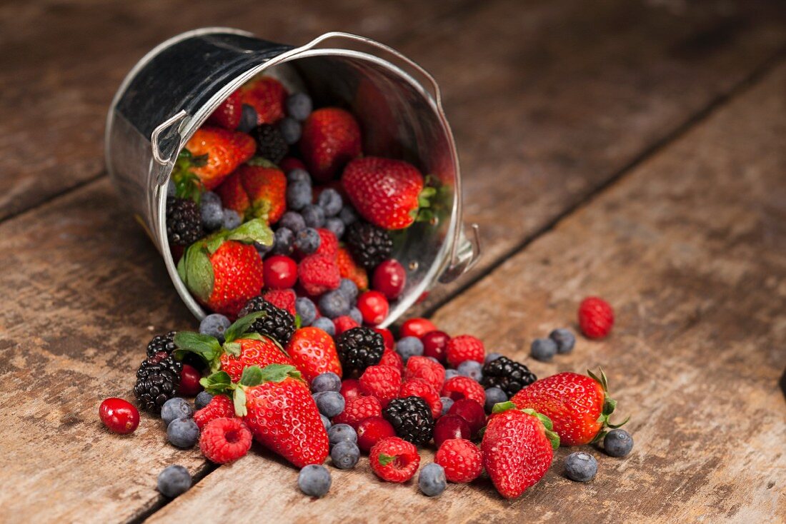 An Overturned Pail of Mixed Berries on Wood