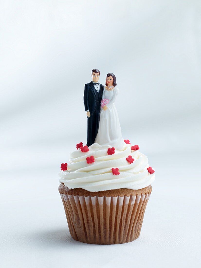 A cupcake topped with a bride and groom