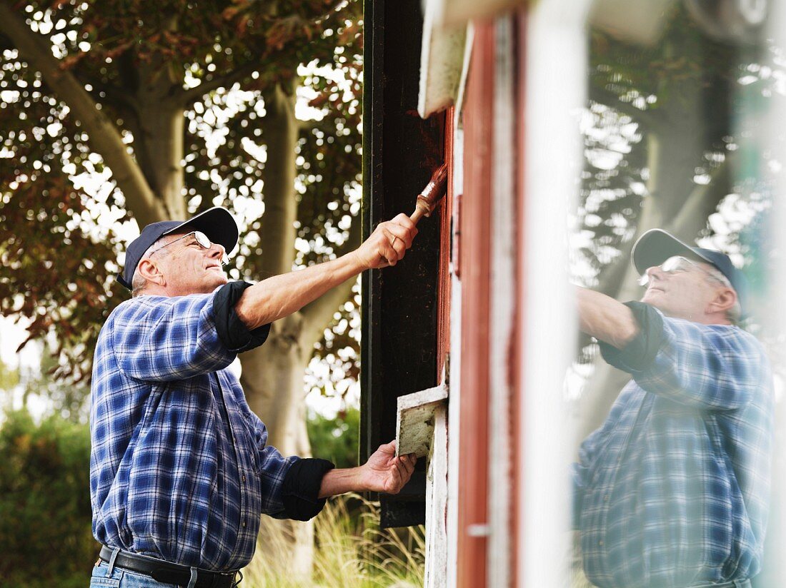 Älterer Mann streicht die Aussenfassade vom Sommerhaus
