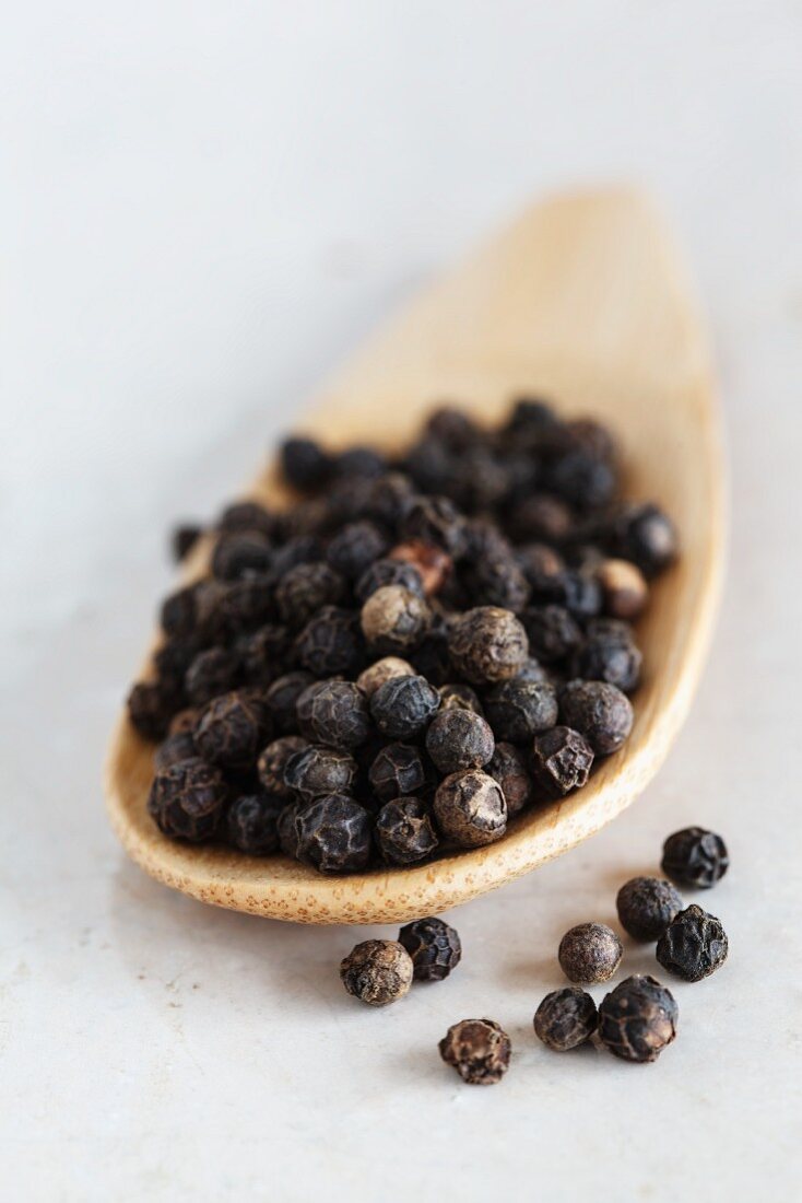 Black peppercorns on a wooden spoon