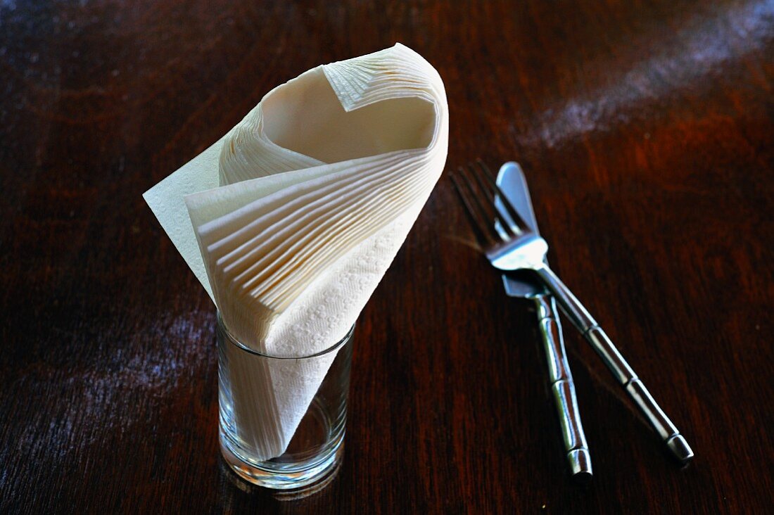 Cutlery and paper napkins in a glass on a wooden table
