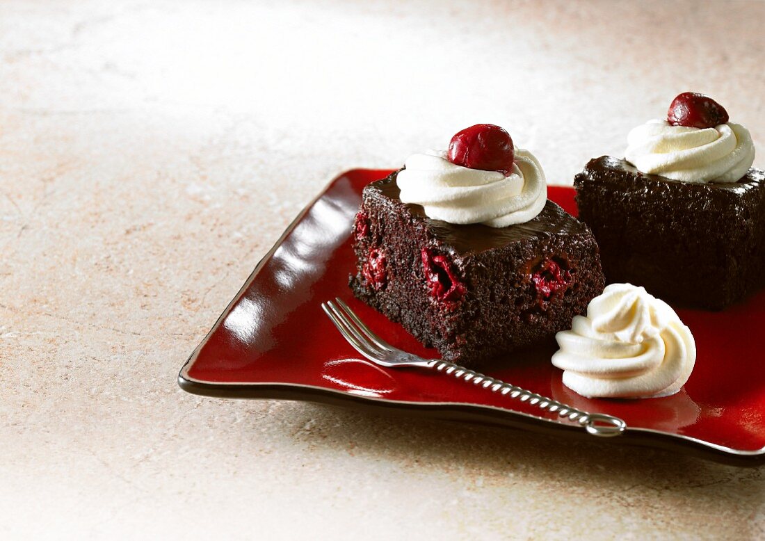 Two slices of chocolate cake with cherries and cream