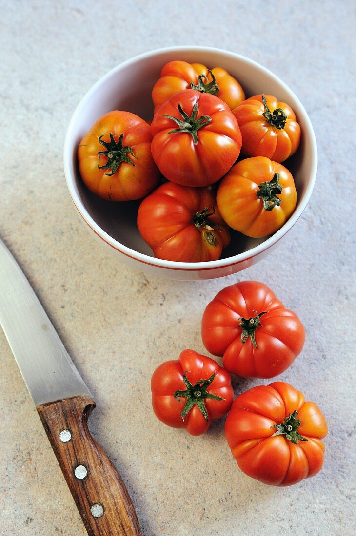 Fresh tomatoes in and next to a bowl with a knife