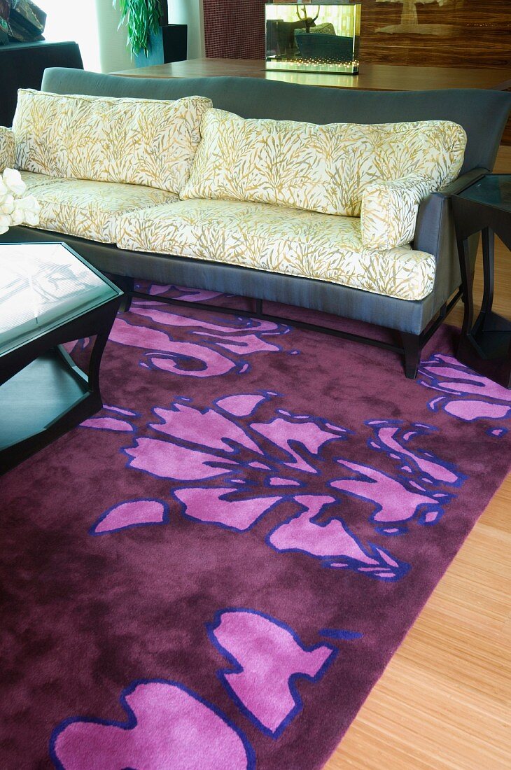 Sofa mit Kissen im Bambusblatt-Design und auffällig gemusterter Teppich in Lila/Pink
