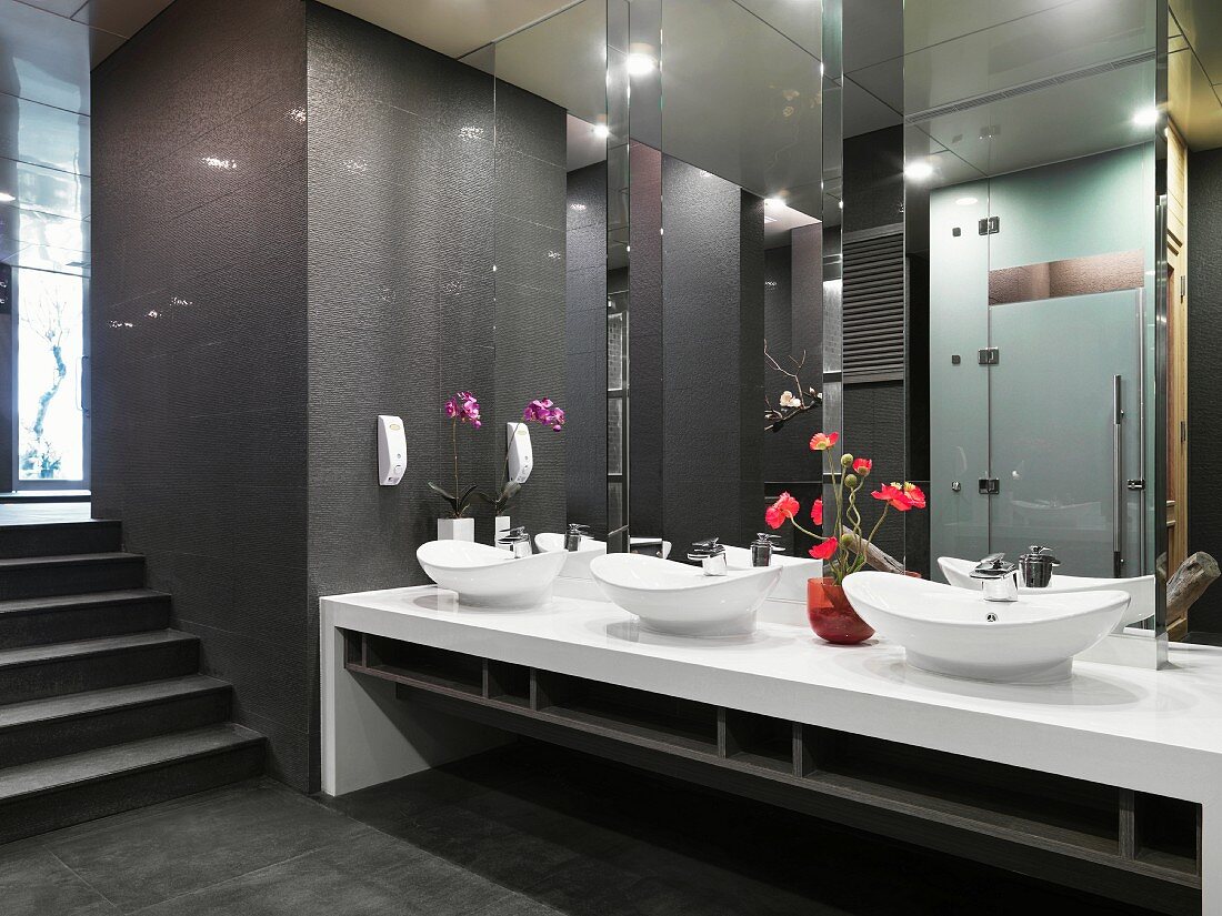 Spiegelfronten über ovalen Waschschüsseln und Blumenschmuck im dunkel getönten, asiatisch modernen Toiletten-Vorraum
