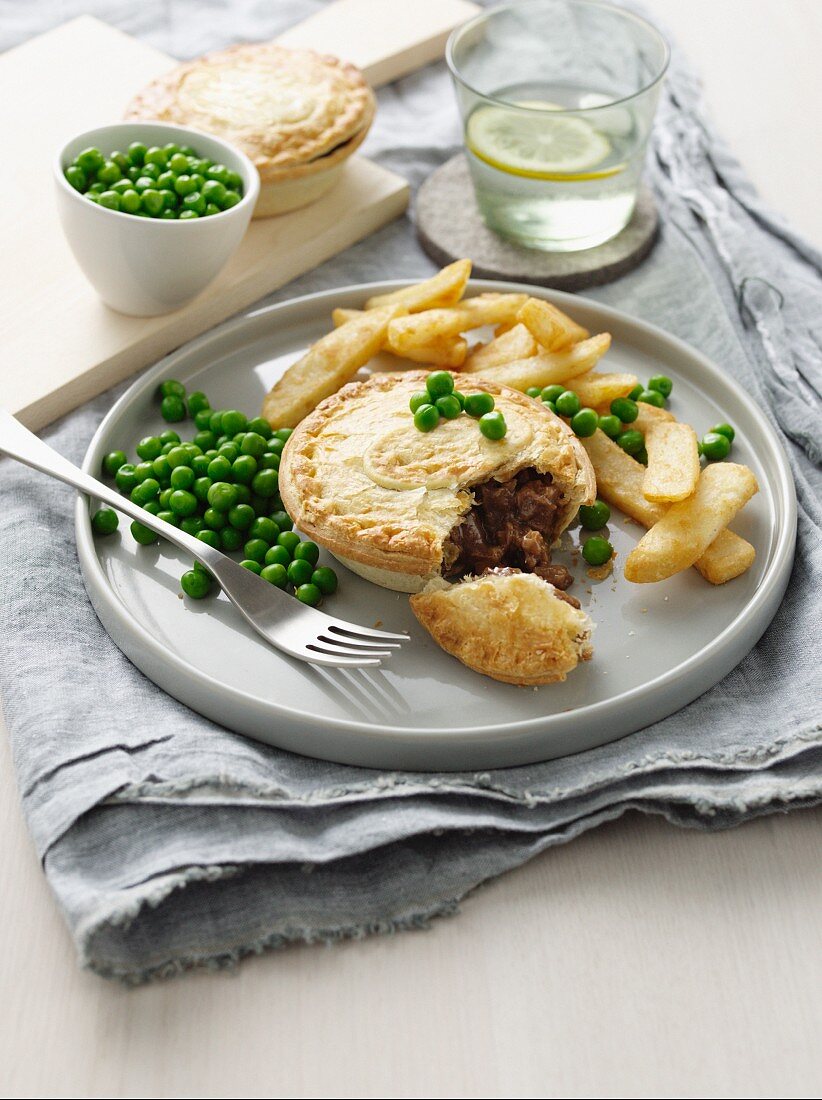 Plate of meat pie, chips and peas