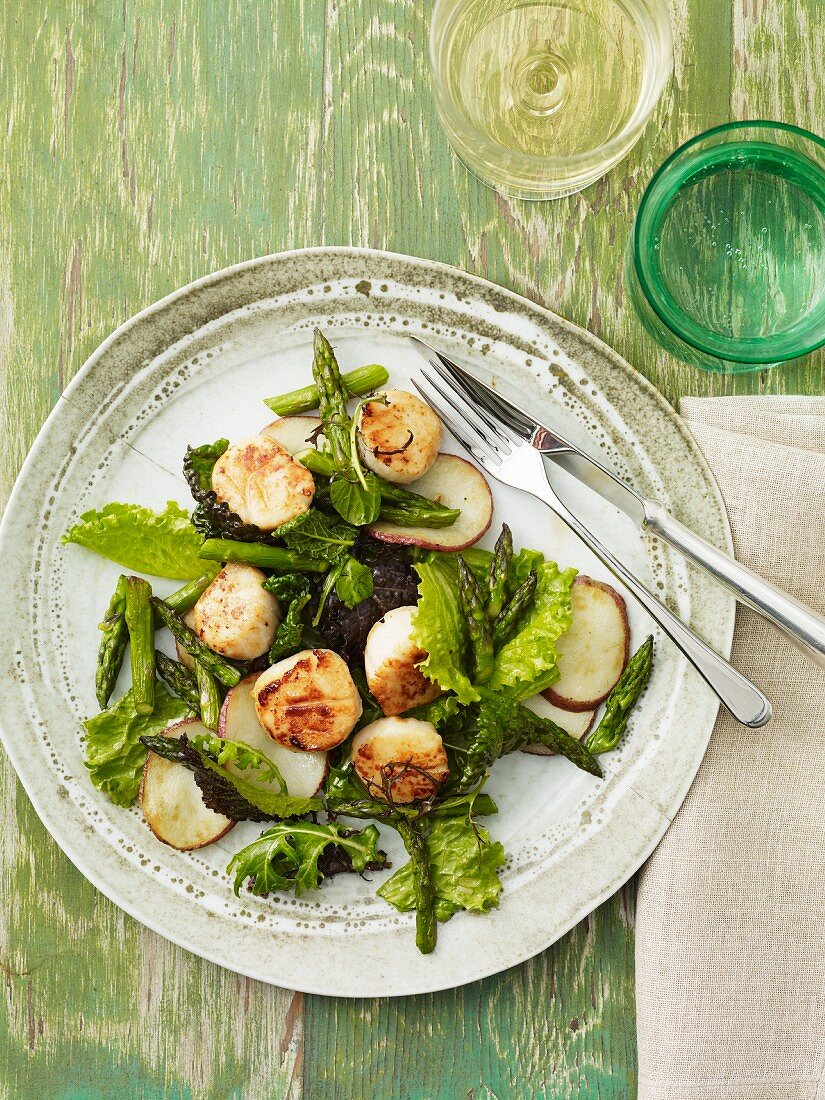 Scallops with Greens and Sliced Potatoes on a Plate; Fork and Knife