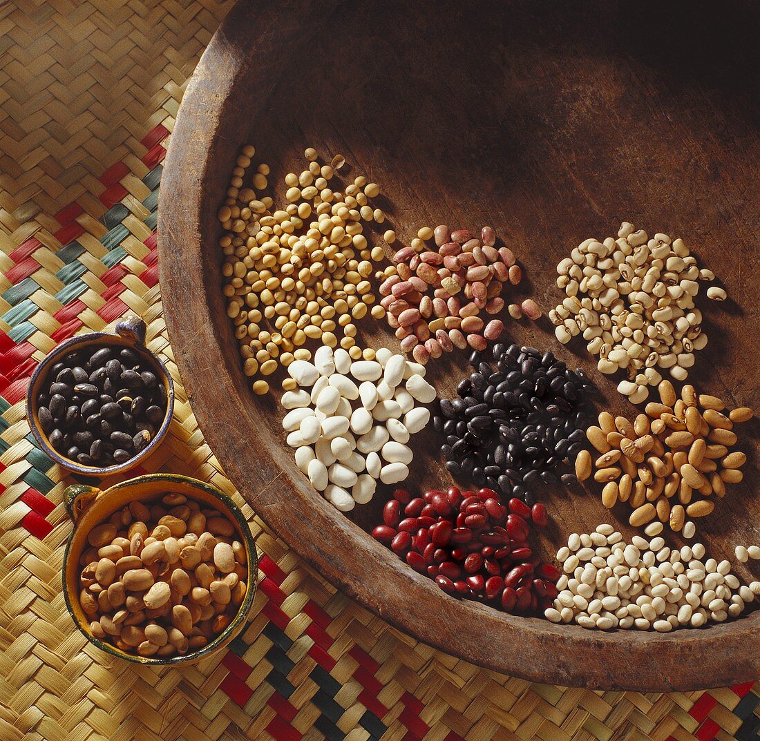 Various types of beans on wooden tray and in bowls