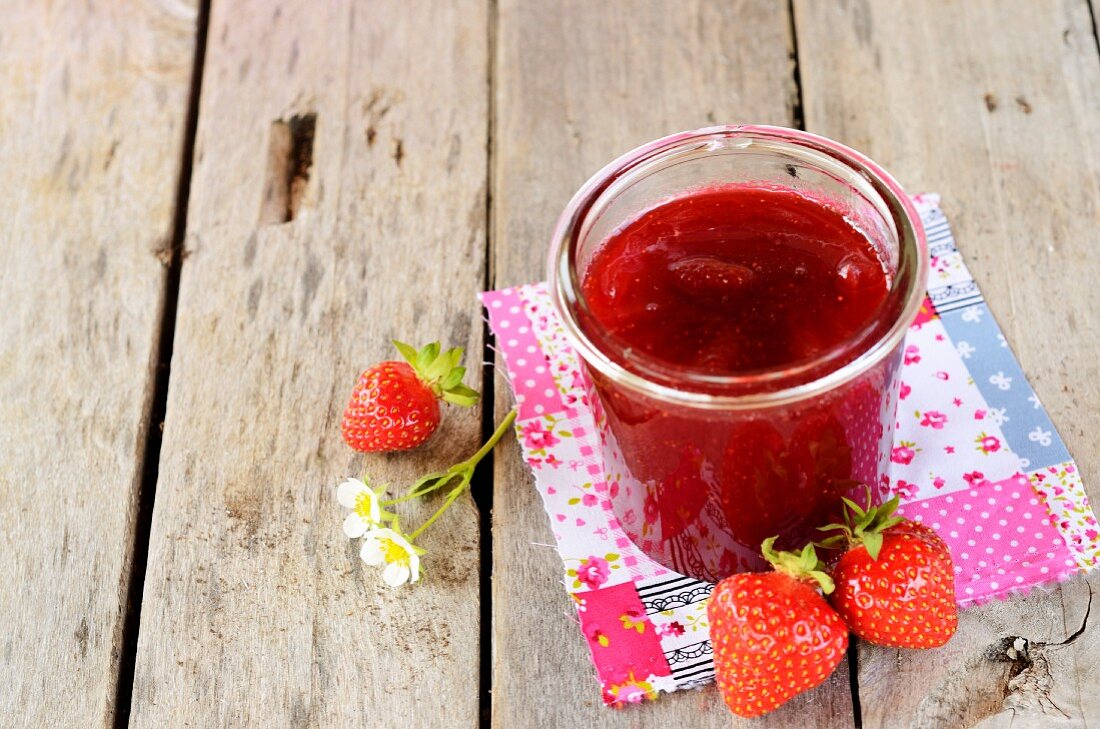 A jar of strawberry jam and fresh strawberries