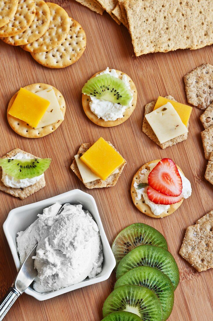 Verschiedene Cracker mit Frischkäse, Cheddar & Früchten belegt