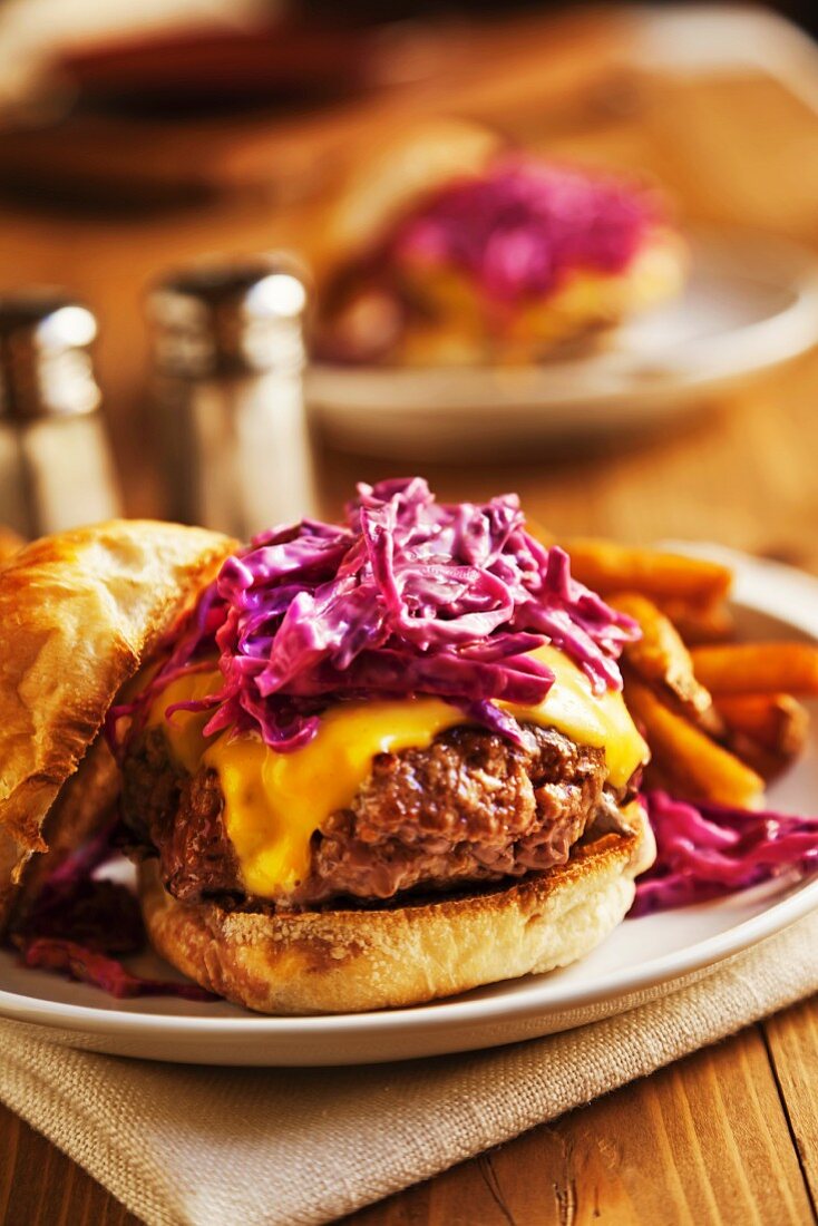 A Cheeseburger topped with red cabbage cole slaw on a plate with french fries