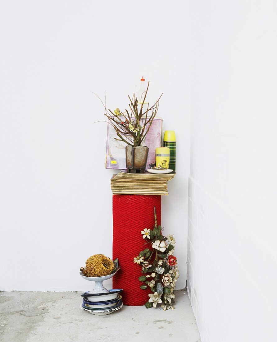 Vase mit Blumenzweigen neben Aufbewahrungsdosen auf gerolltem rotem Teppich neben Vintage Metall Schalen auf Betonboden