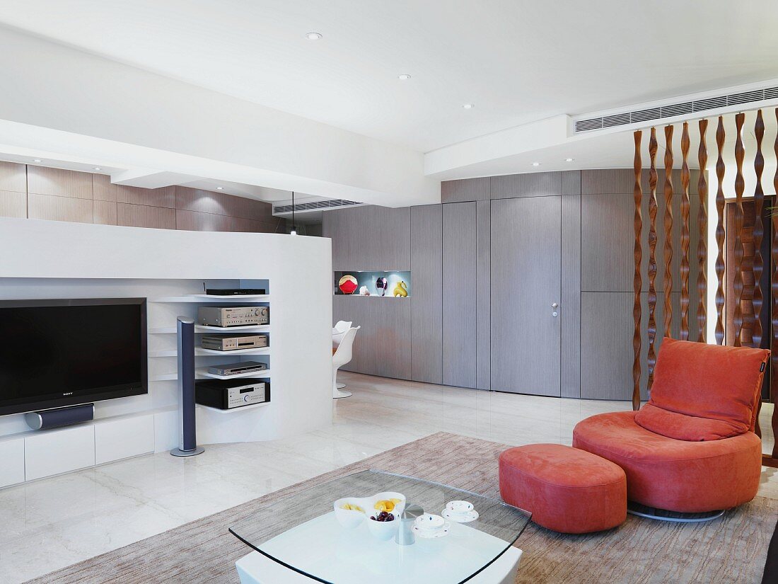 Modern living room with a lounger upholstered in pink and matching ottoman across from a room partition with a built in TV