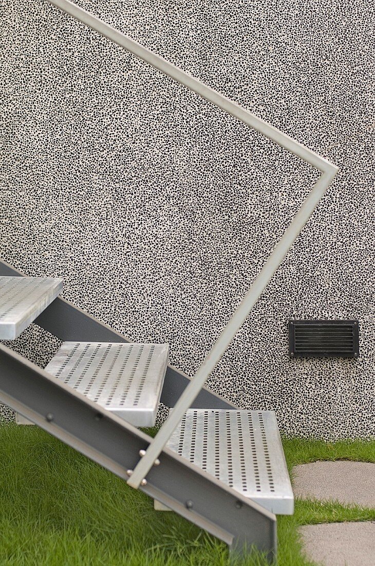 Minimalistische Treppe aus Metall auf Grasboden vor grauer Hausfassade