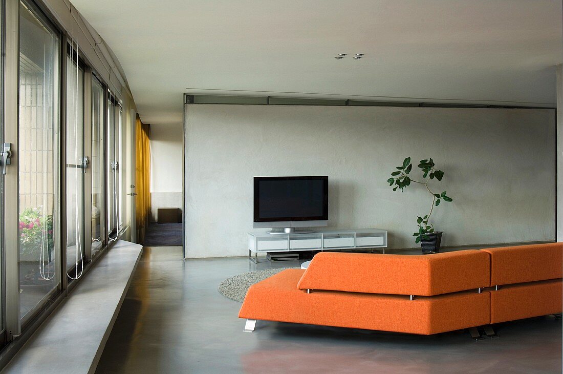 Designer Couch in Orange gegenüber dem Fernseher auf Hifiregal in minimalistischem Wohnzimmer