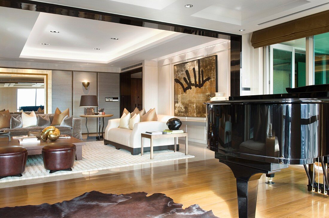 Klavierflügel im offenen Vorraum und Blick auf elegante Polstermöbel im Wohnraum mit indirekter Deckenbeuchtung