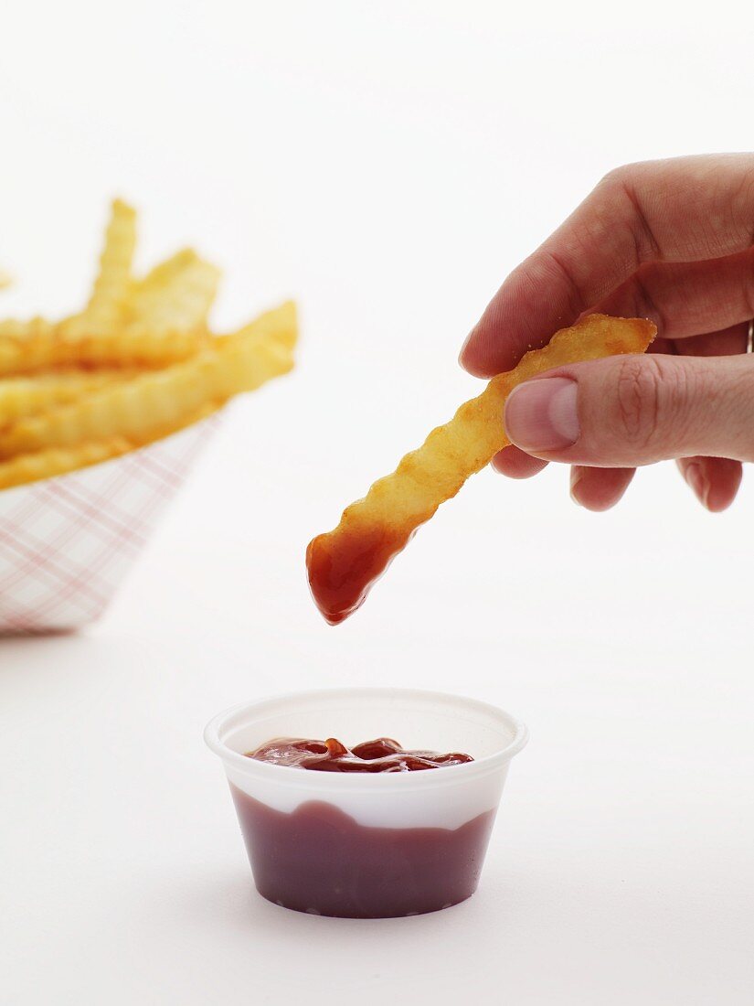 Hand dippt Pommes Frites in Ketchup