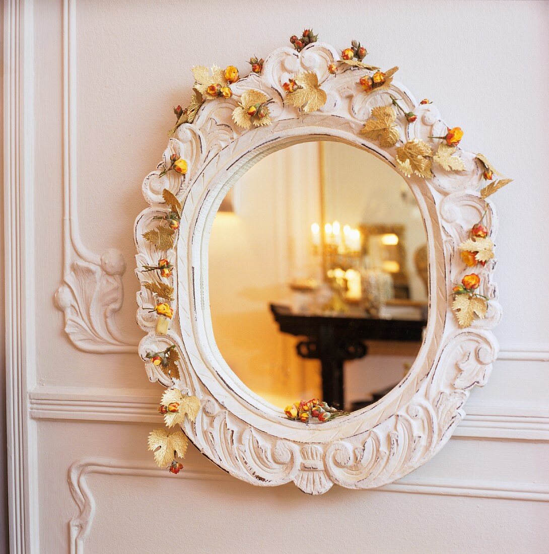 Reflection in wall mirror with floral garland on white, carved frame on white wooden wall panel
