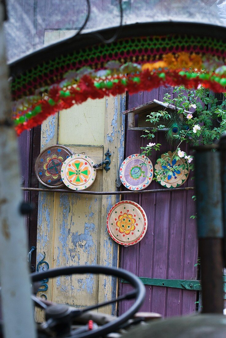 View through vehicle windscreen of round chopping boards painted with colourful patterns leaning on purple painted wooden door