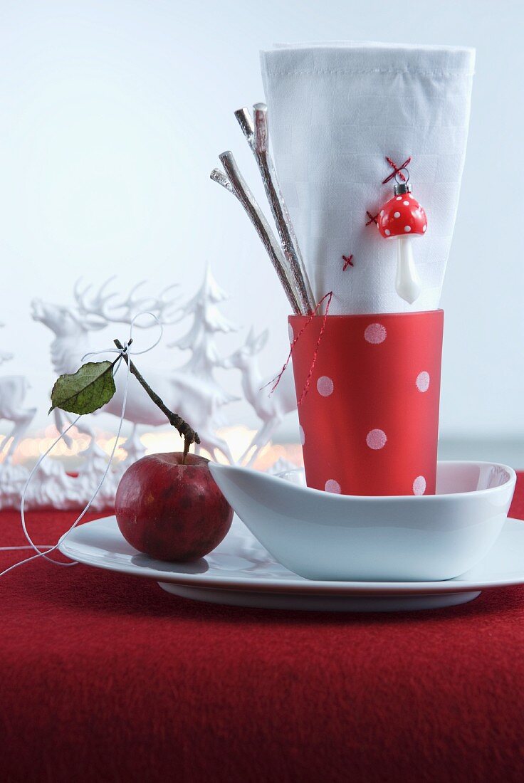 Red and white napkin in red beaker with white polka dots in white bowl on red felt cloth