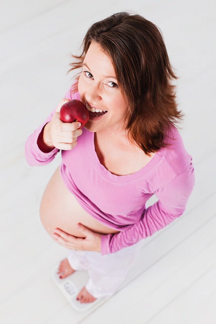 Schwangere Frau isst einen Apfel auf der Waage