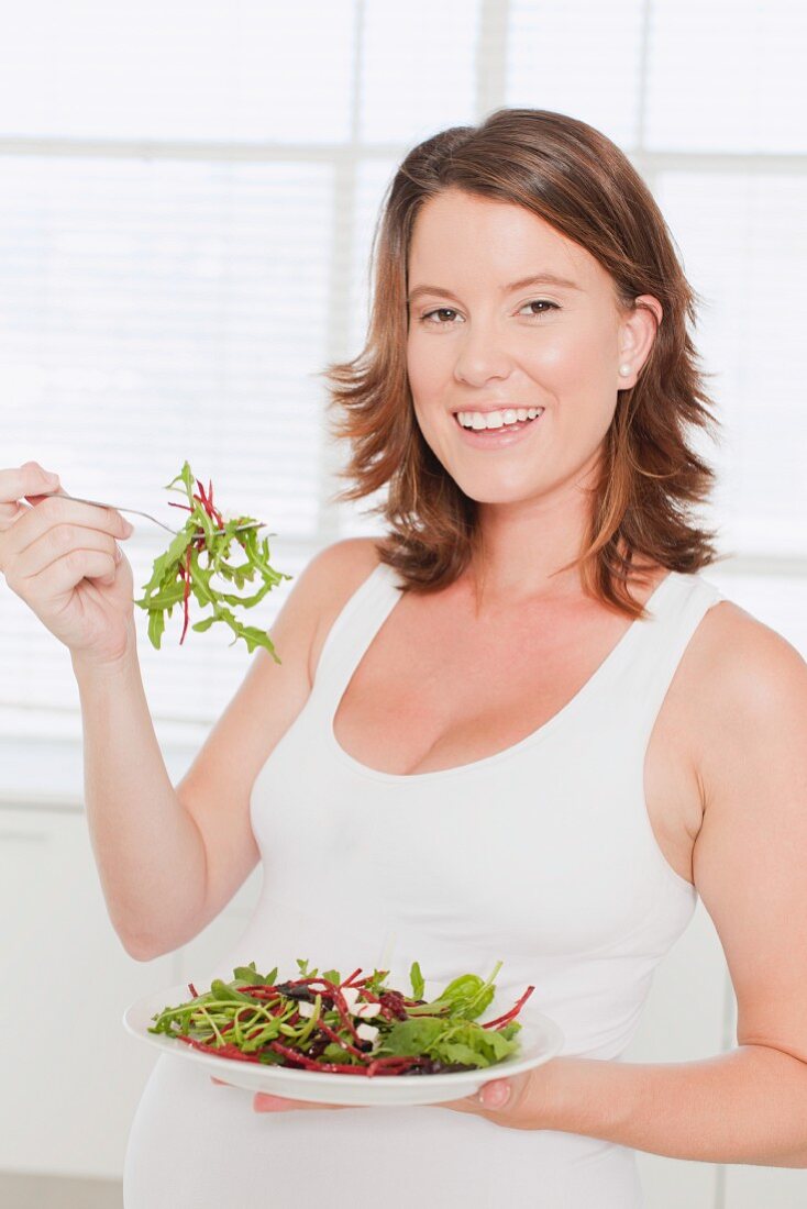 Pregnant woman eating salad in kitchen