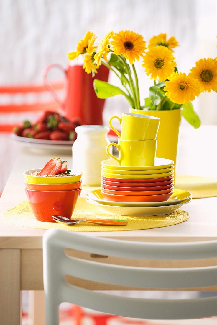 Colourful teacups and bowls on table in front of yellow flowers