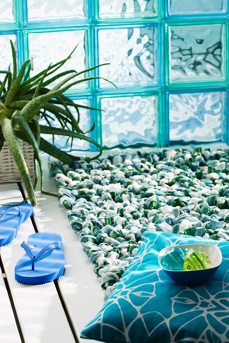 Grün-weiße Badematte mit Schlaufen vor türkisfarbenen Glasbausteinen