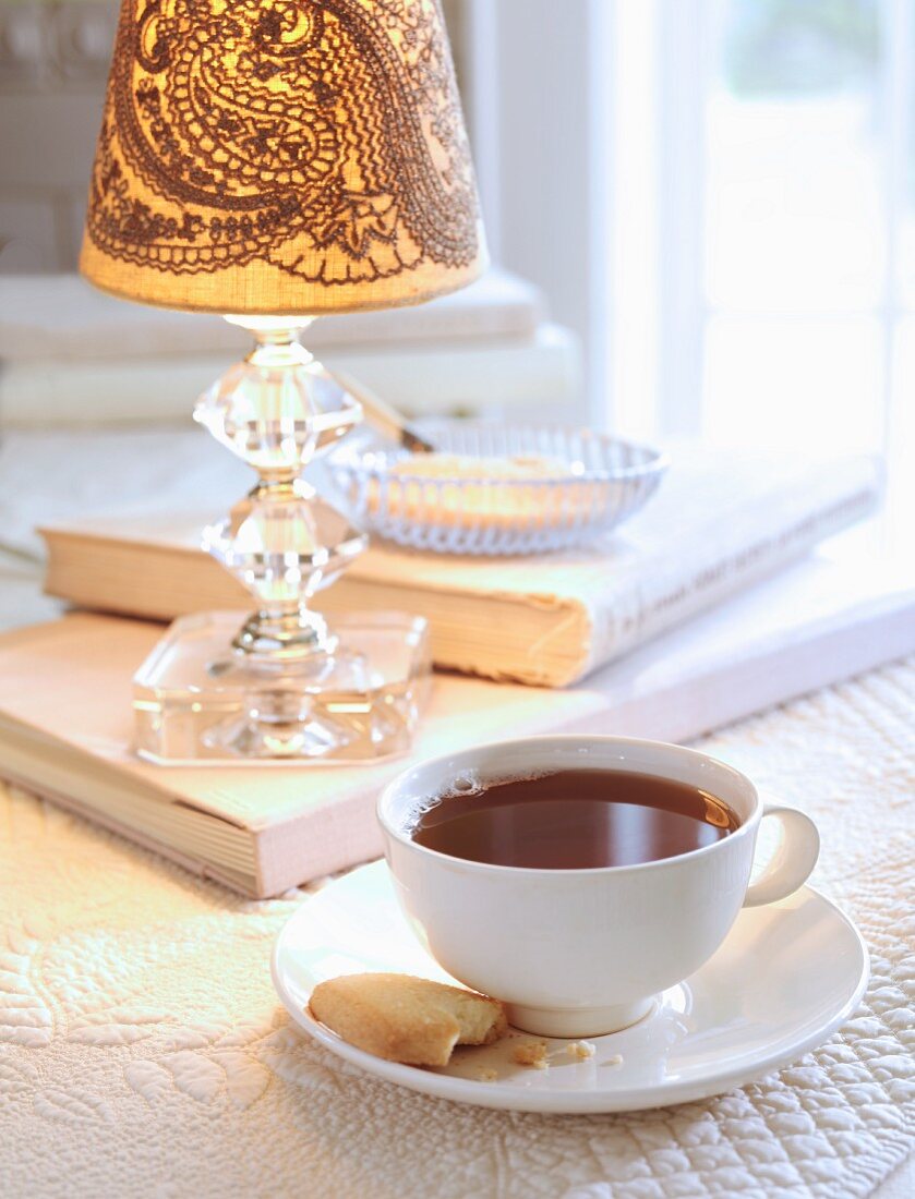 Eine Tasse Tee mit Keks auf Tisch mit Tischleuchte & Büchern