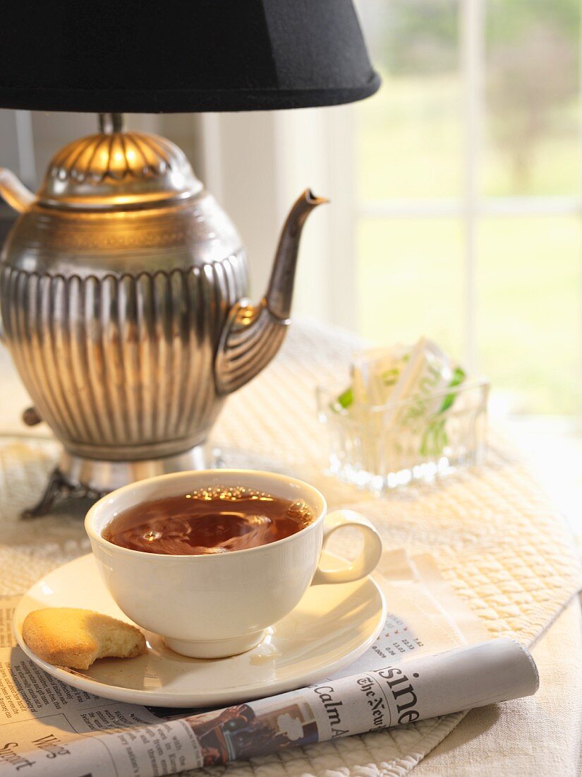 Eine Tasse Tee mit Keks auf Tisch mit teekannenförmiger Lampe