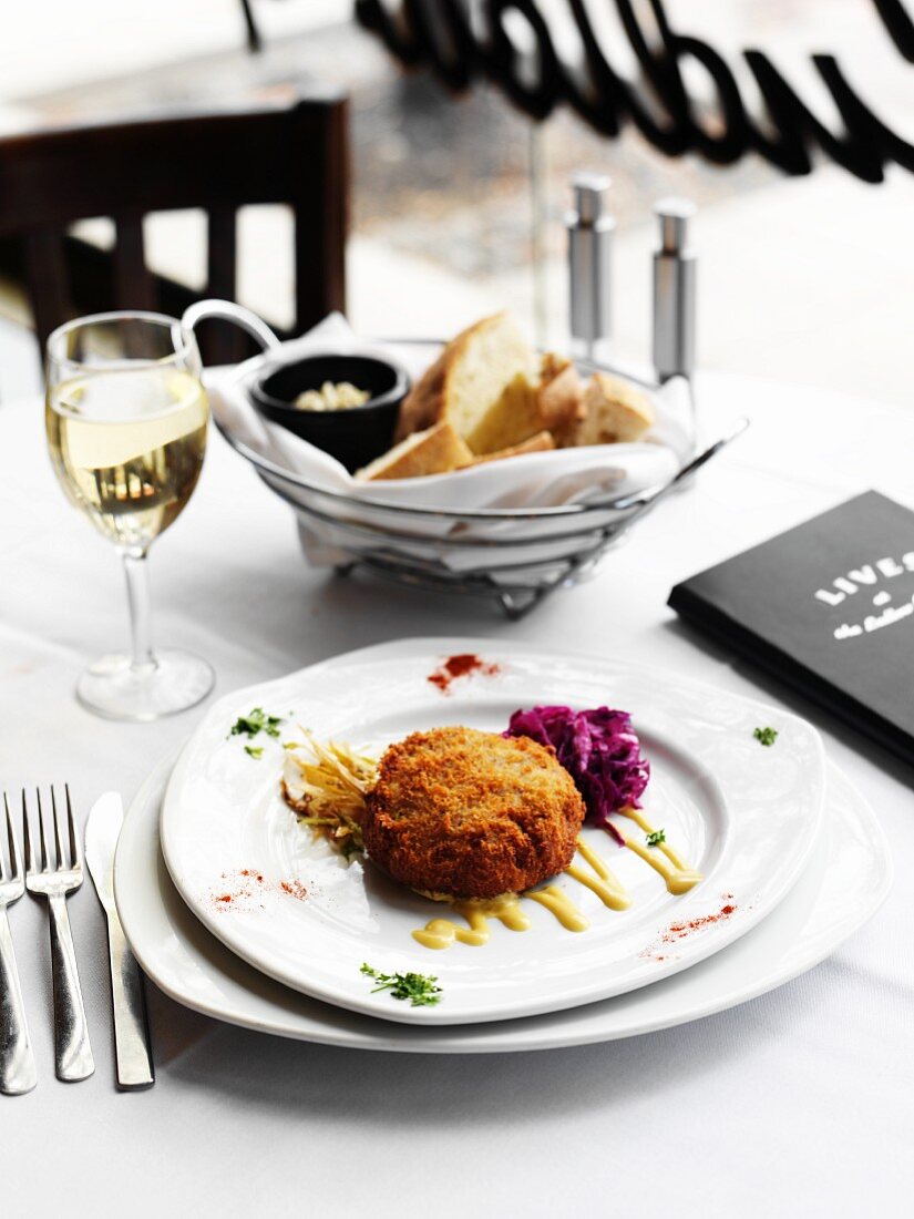 Crab Cake mit Glas Wein & Brot im Korb auf Restauranttisch