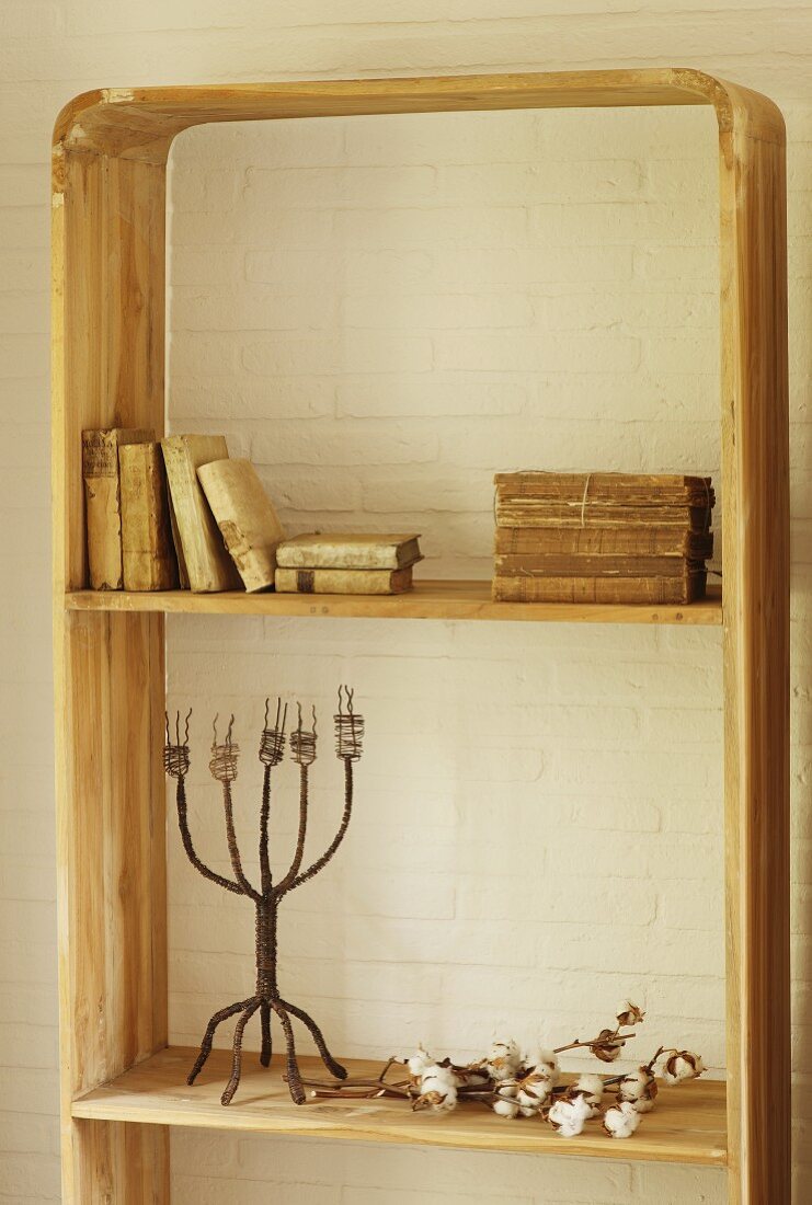 Antiquarian books and vintage candlestick on rustic wooden shelving against whitewashed brick wall