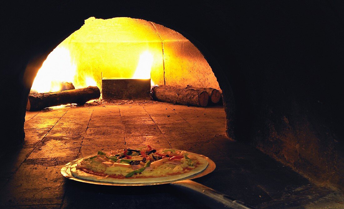 A pizza being placed in a wood-fired oven