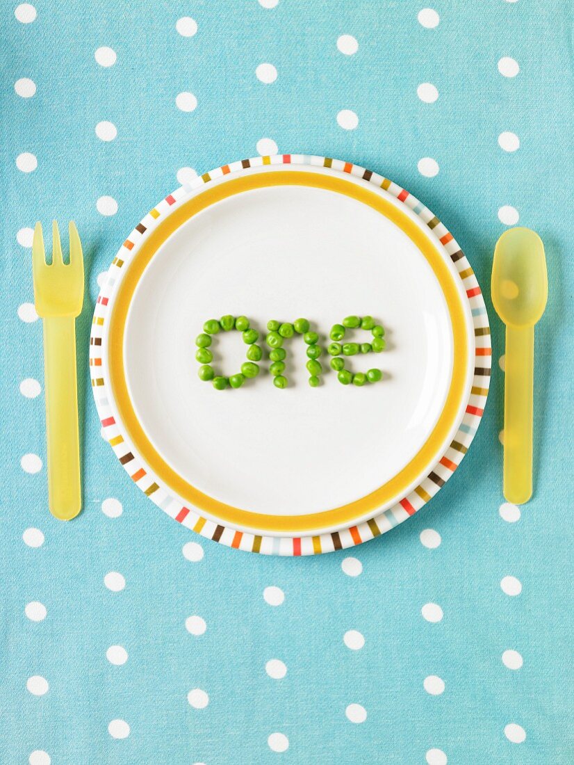 The word "one" spelled out with peas on a plate