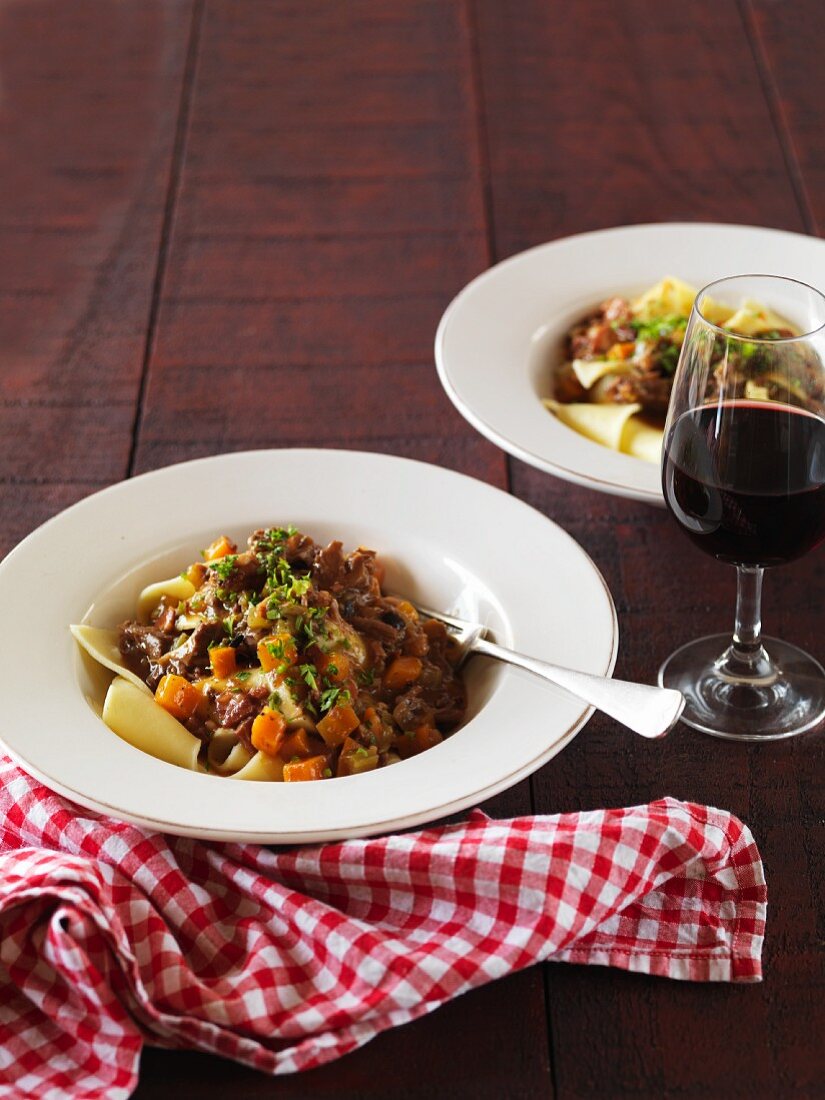 Lamb ragout with rosemary on a bed of pasta with a glass of red wine