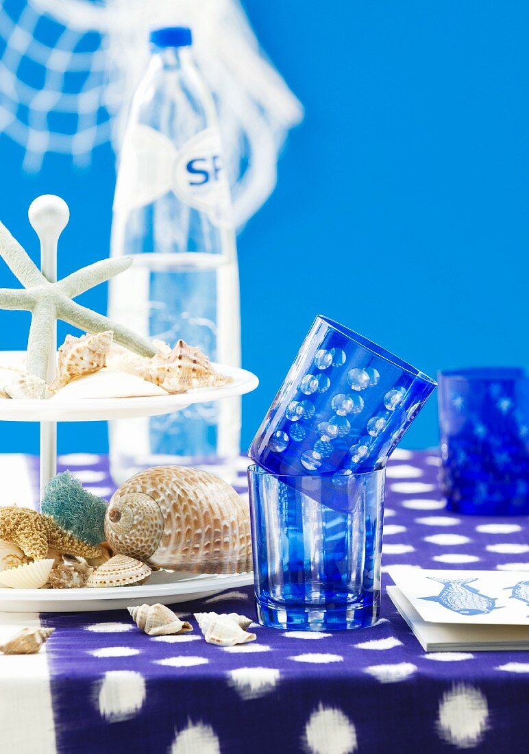 Tisch mit blauer Tischdecke, blauen Trinkgläsern & Muscheln auf Etagere