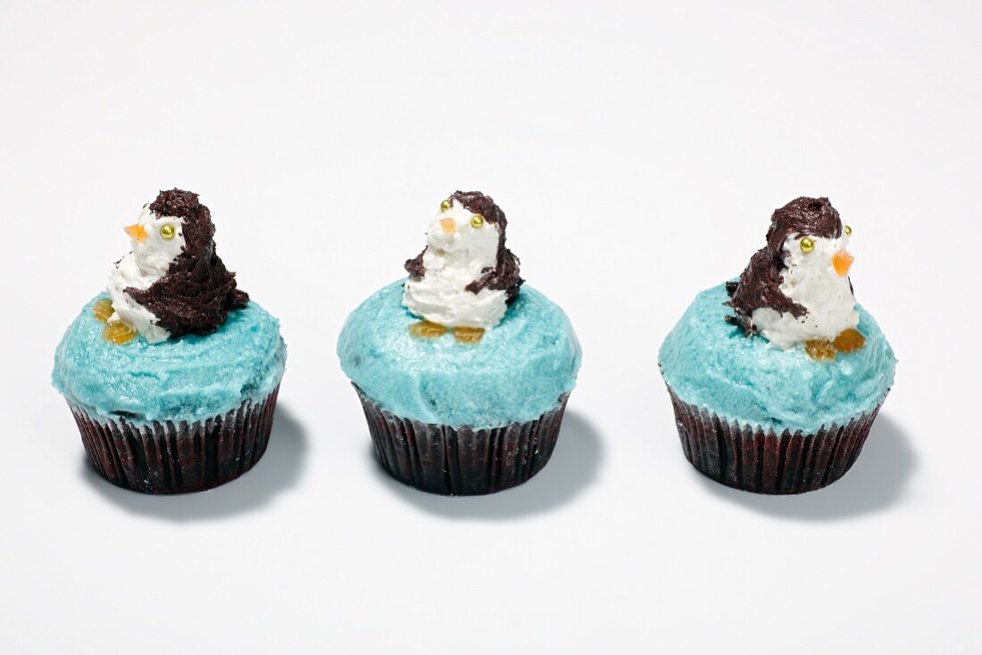 Three cupcakes decorated with penguins on a white surface