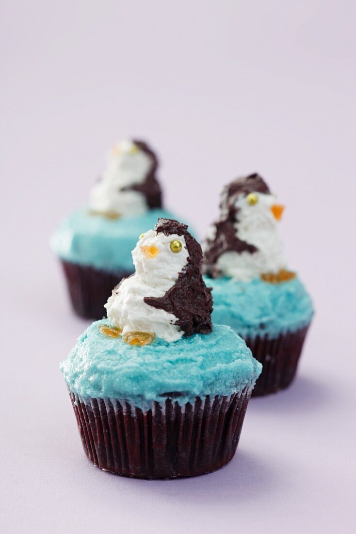 Three cupcakes decorated with penguins on a purple surface