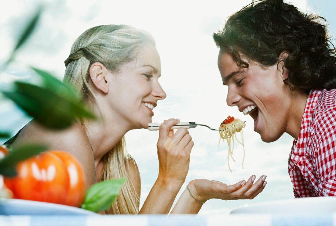 A young woman feeding her boyfriend spaghetti