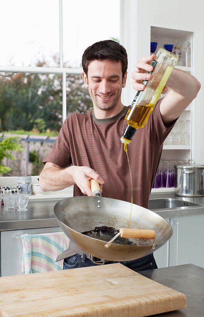 Mann giesst Olivenöl in einen Wok