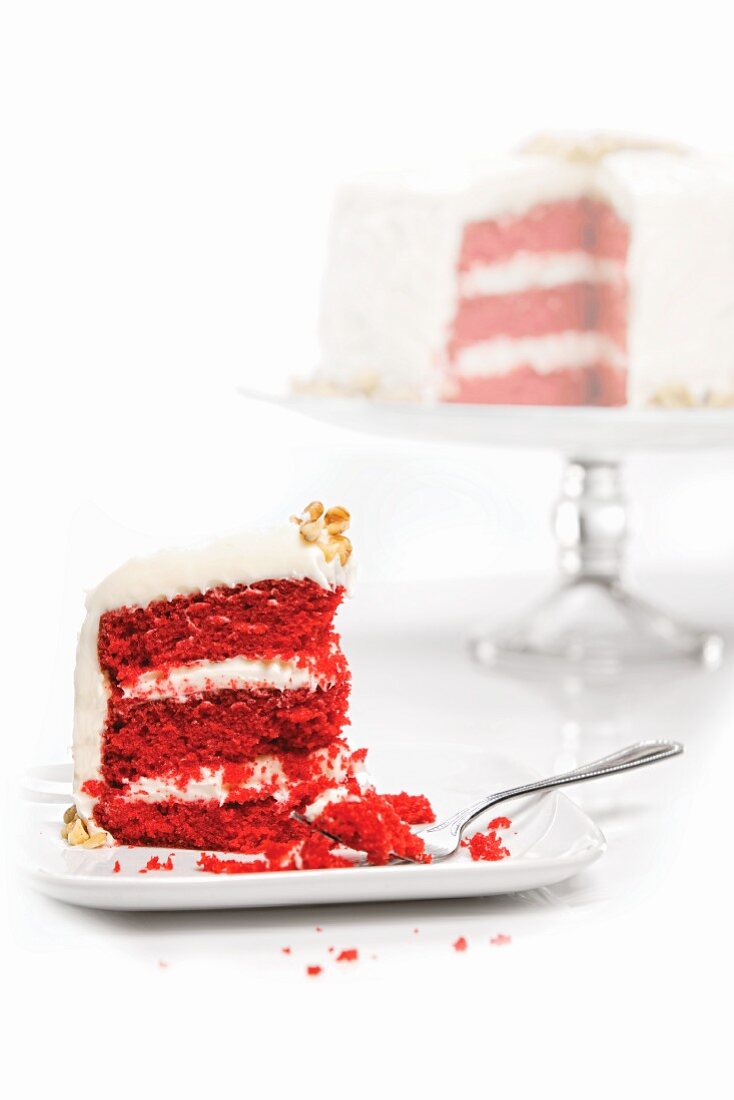Slice of Red Velvet Cake On a Plate with Whole Cake in Background
