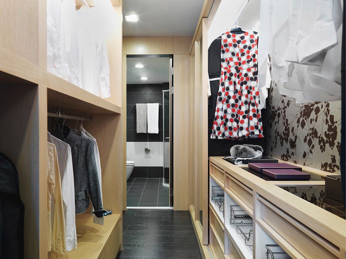 Open cupboard in a dressing room with a view through a open door into a bathroom